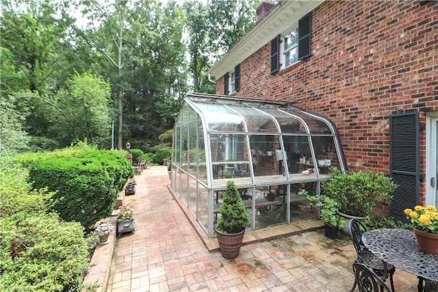 view of side of home with a sunroom, brick siding, a patio, and a chimney