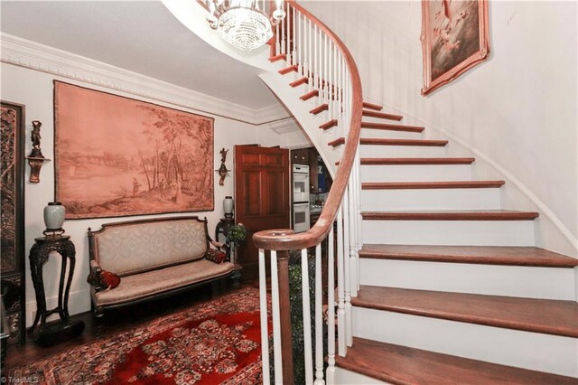 stairway with an inviting chandelier, ornamental molding, and hardwood / wood-style floors