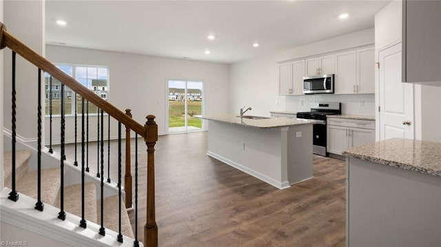 kitchen featuring stainless steel appliances, light stone counters, dark hardwood / wood-style flooring, an island with sink, and white cabinets