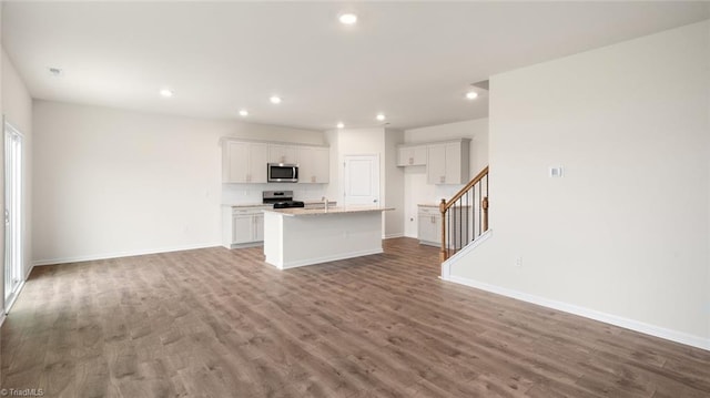 kitchen with wood-type flooring, a center island with sink, white cabinetry, and stainless steel appliances