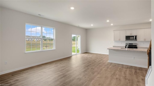 kitchen with light stone countertops, light wood-type flooring, stainless steel appliances, a center island with sink, and white cabinets