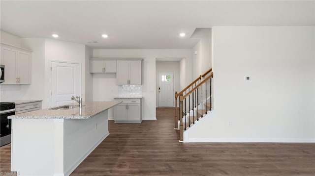 kitchen featuring sink, an island with sink, appliances with stainless steel finishes, dark hardwood / wood-style flooring, and light stone counters