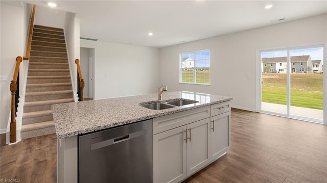 kitchen with dishwasher, sink, light stone counters, light hardwood / wood-style floors, and a center island with sink