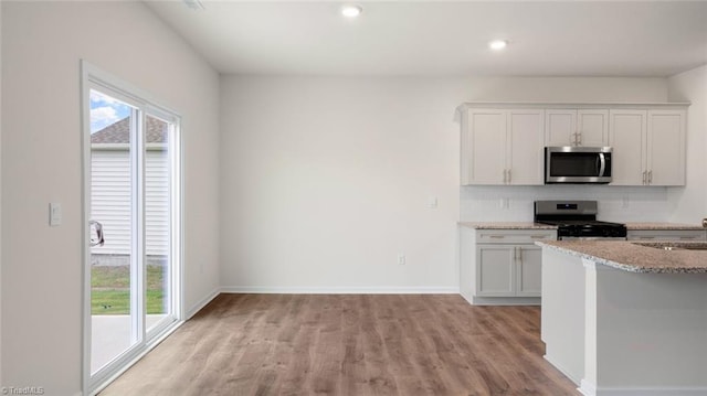 kitchen featuring light stone countertops, white cabinets, light wood-type flooring, and appliances with stainless steel finishes