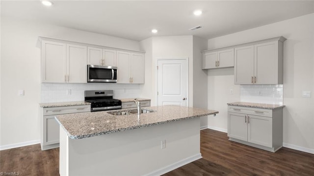 kitchen with dark hardwood / wood-style flooring, stainless steel appliances, light stone counters, and a kitchen island with sink