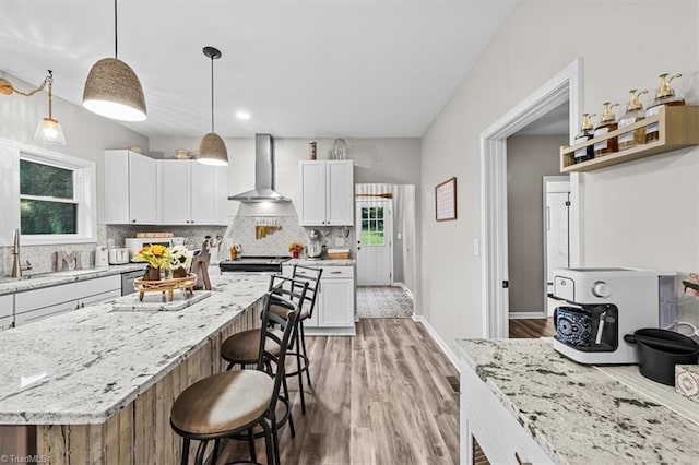 7517 NC Highway 62, Trinity, NC 27370 - kitchen with wall chimney range hood, a kitchen bar, light wood-style flooring, and decorative backsplash