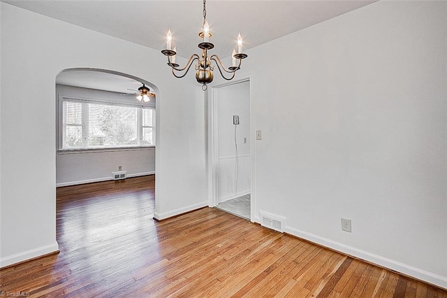 unfurnished dining area featuring ceiling fan with notable chandelier and wood-type flooring