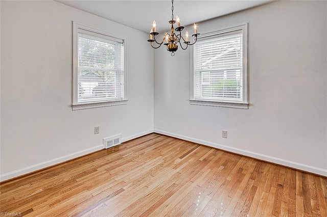 spare room featuring a chandelier, a wealth of natural light, and light hardwood / wood-style flooring