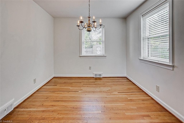 empty room with a wealth of natural light, a notable chandelier, and light hardwood / wood-style floors