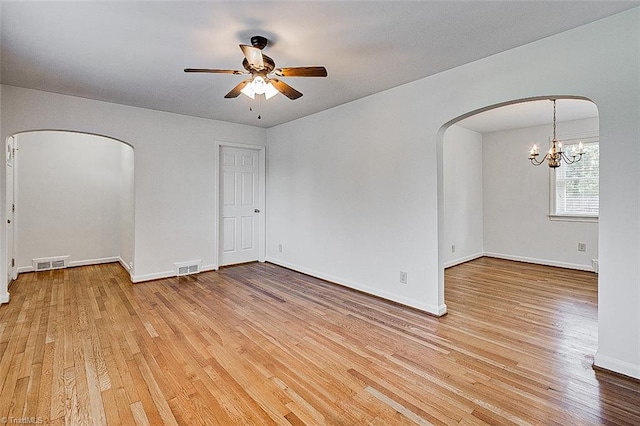 empty room with ceiling fan with notable chandelier and light hardwood / wood-style flooring