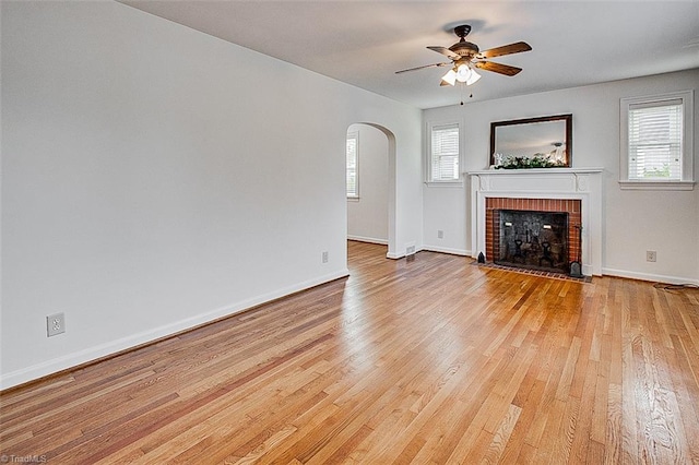 unfurnished living room with light wood-type flooring, ceiling fan, a brick fireplace, and plenty of natural light