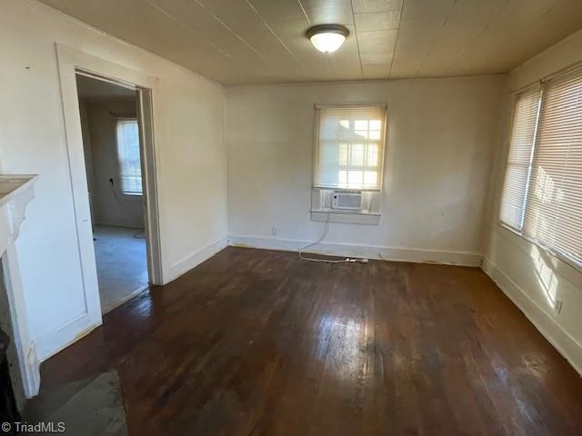 empty room with cooling unit, a healthy amount of sunlight, and dark hardwood / wood-style floors