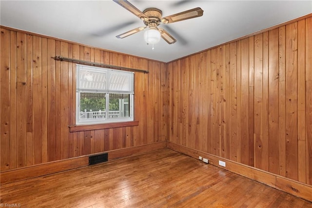 empty room with ceiling fan, wood walls, and wood-type flooring