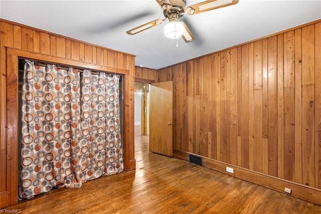 spare room featuring wood-type flooring, wooden walls, and ceiling fan