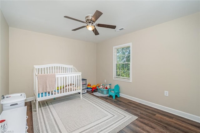 bedroom featuring ceiling fan, a crib, and dark wood-type flooring