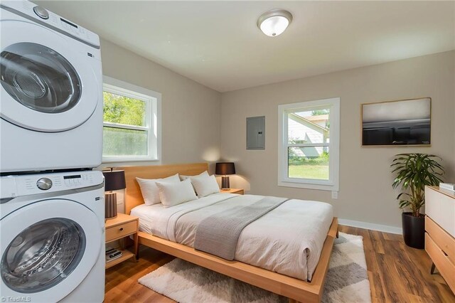 bedroom with baseboards, stacked washer / dryer, wood finished floors, and electric panel