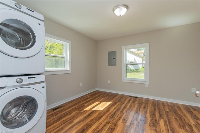 washroom featuring stacked washer / drying machine, laundry area, wood finished floors, electric panel, and baseboards