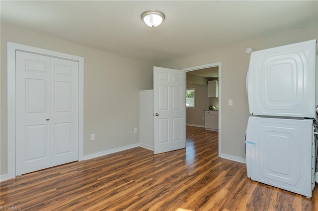 unfurnished bedroom featuring stacked washer and clothes dryer, a closet, baseboards, and dark wood-style flooring