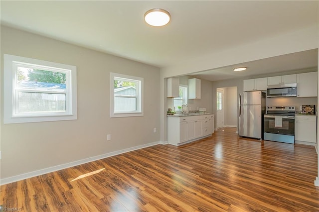 kitchen with baseboards, a sink, appliances with stainless steel finishes, and dark wood-style flooring