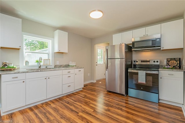 kitchen with white cabinets, light stone counters, wood finished floors, a sink, and appliances with stainless steel finishes
