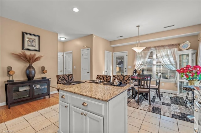 kitchen featuring hanging light fixtures, light tile patterned flooring, light stone countertops, and a kitchen island