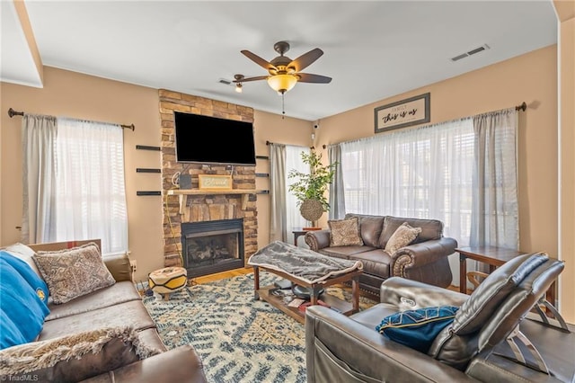 living room featuring a stone fireplace, visible vents, a healthy amount of sunlight, and a ceiling fan