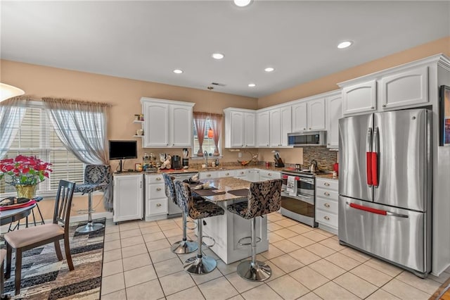 kitchen featuring a kitchen island, light tile patterned flooring, appliances with stainless steel finishes, white cabinetry, and a kitchen bar