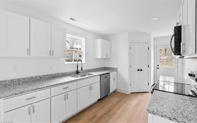 kitchen featuring light wood-type flooring, light stone counters, stainless steel dishwasher, sink, and white cabinets