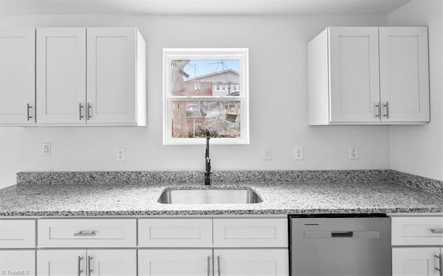 kitchen with stainless steel dishwasher, light stone counters, white cabinets, and sink