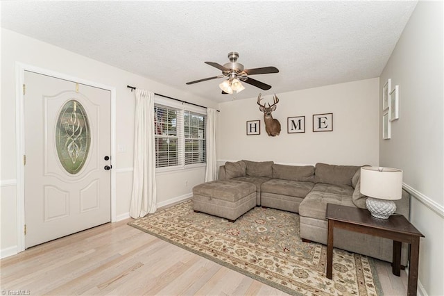 living room featuring light hardwood / wood-style flooring, ceiling fan, and a textured ceiling