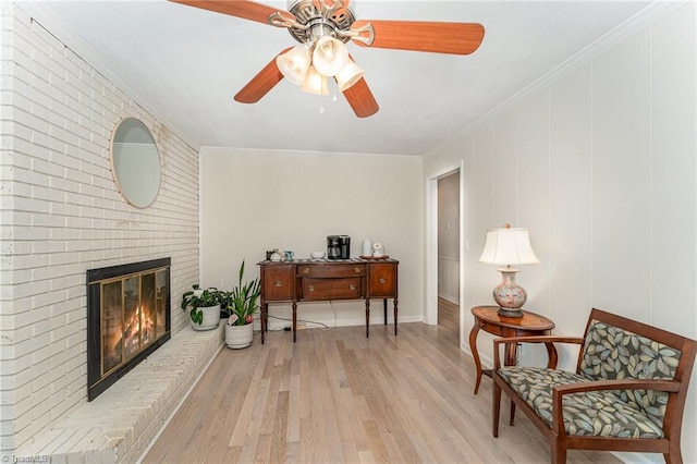 living area featuring ornamental molding, light wood-type flooring, ceiling fan, and a fireplace