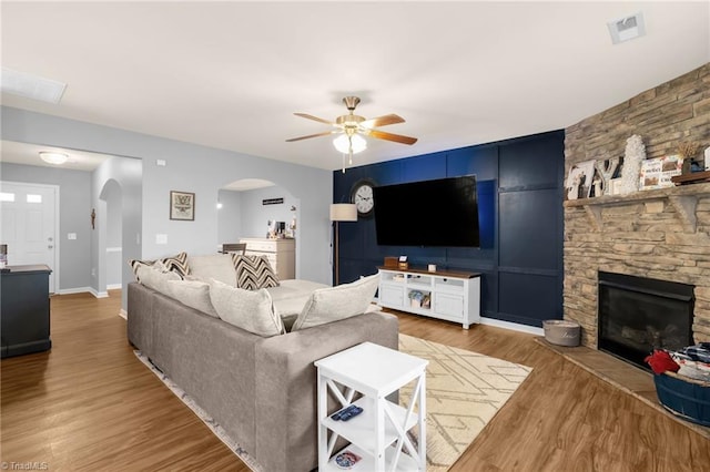 living room featuring wood-type flooring, a stone fireplace, and ceiling fan