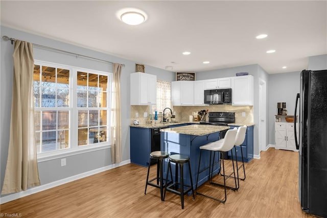 kitchen featuring backsplash, black appliances, light hardwood / wood-style flooring, a center island, and white cabinetry