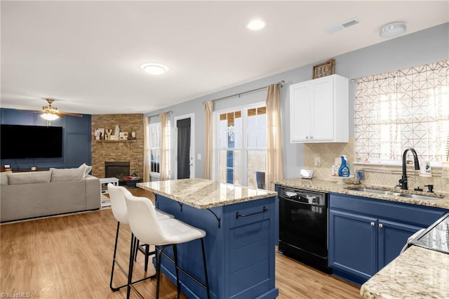 kitchen featuring white cabinets, a stone fireplace, sink, blue cabinetry, and black dishwasher