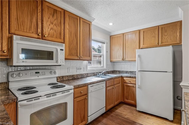 kitchen featuring white appliances, dark countertops, wood finished floors, crown molding, and a sink