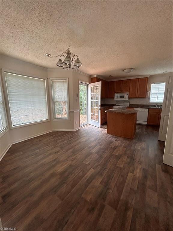 kitchen featuring white appliances, a kitchen island, open floor plan, dark countertops, and dark wood finished floors