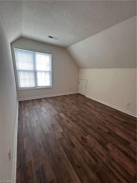 additional living space featuring a textured ceiling, vaulted ceiling, dark wood-style floors, and visible vents