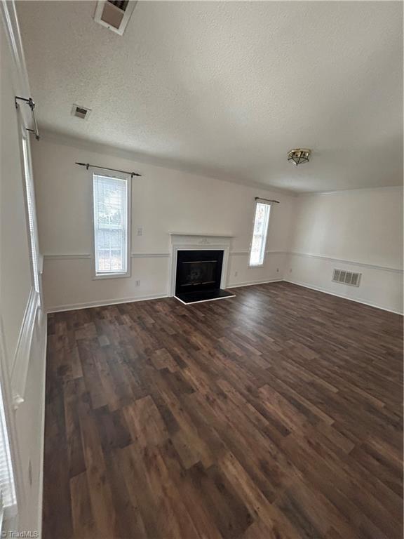 unfurnished living room featuring dark wood-style floors, visible vents, a fireplace with raised hearth, and a textured ceiling