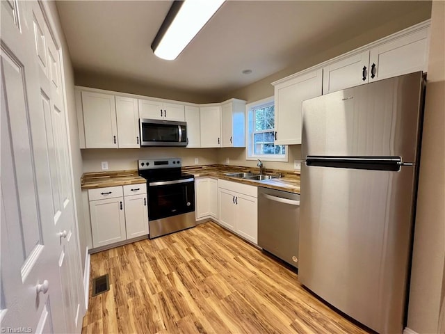 kitchen featuring light wood-style flooring, stainless steel appliances, a sink, visible vents, and white cabinetry