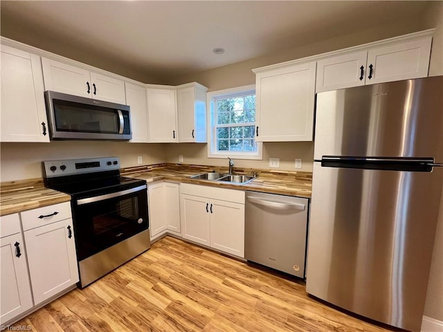 kitchen with appliances with stainless steel finishes, a sink, wood counters, and white cabinets