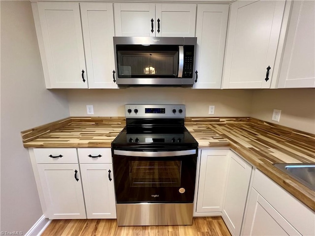 kitchen with electric range oven, butcher block counters, stainless steel microwave, and white cabinetry