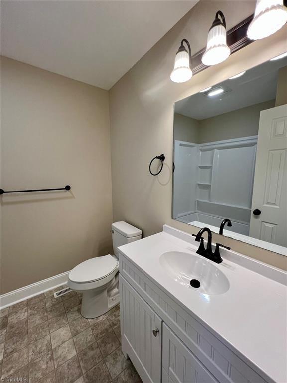 bathroom with visible vents, baseboards, toilet, walk in shower, and vanity