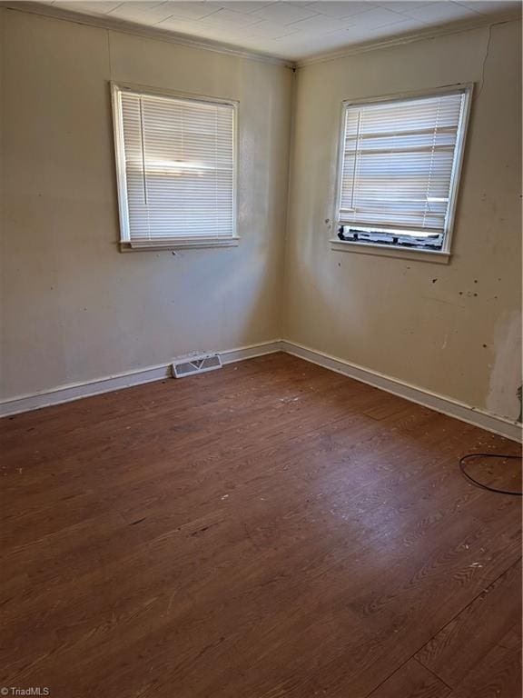 empty room featuring a healthy amount of sunlight, crown molding, and dark hardwood / wood-style floors