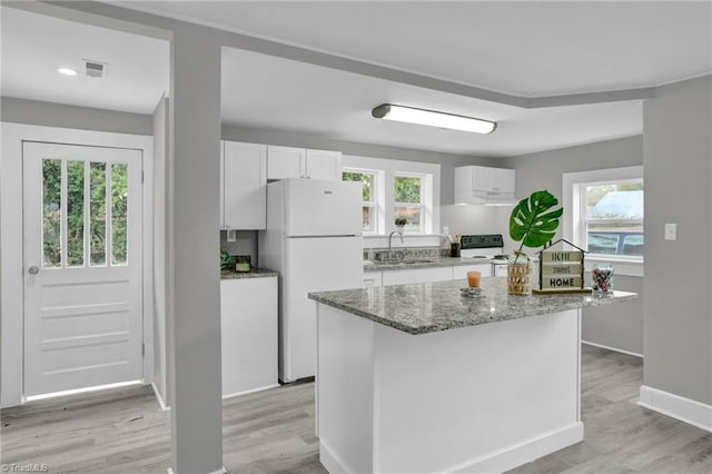 kitchen with a wealth of natural light, white cabinetry, white refrigerator, and light hardwood / wood-style flooring