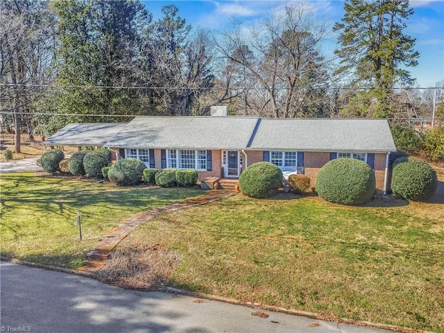 ranch-style home with brick siding, a chimney, and a front lawn