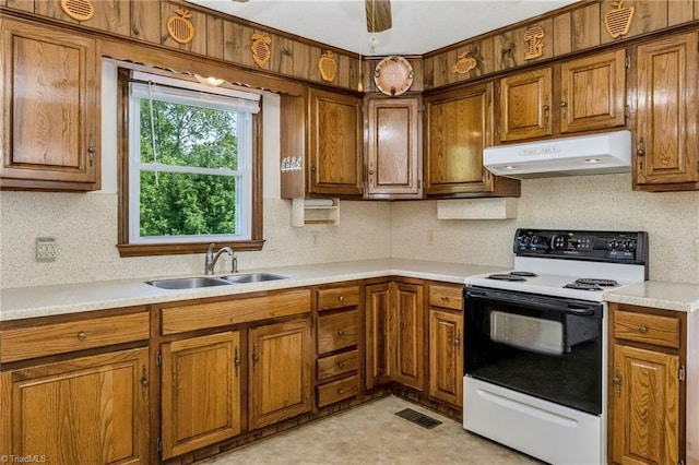 kitchen featuring under cabinet range hood, electric range oven, brown cabinetry, and a sink