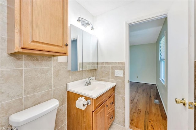half bath with tile walls, toilet, wood finished floors, and vanity