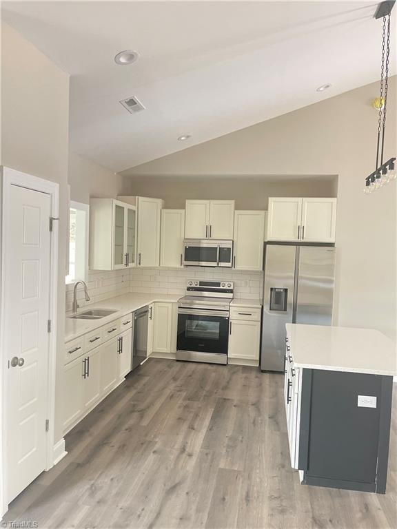 kitchen featuring sink, hardwood / wood-style floors, pendant lighting, vaulted ceiling, and appliances with stainless steel finishes