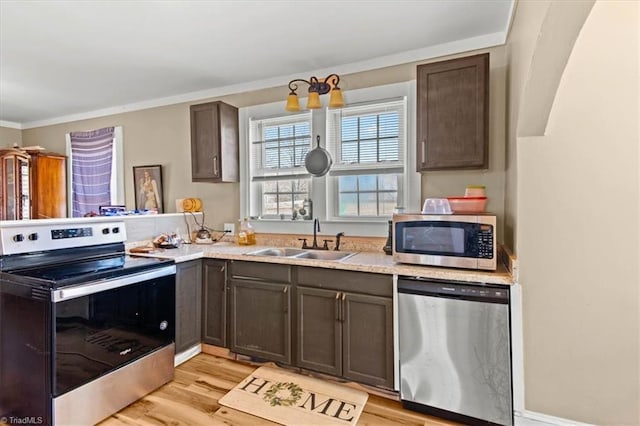 kitchen with a peninsula, a sink, light wood-style floors, appliances with stainless steel finishes, and crown molding