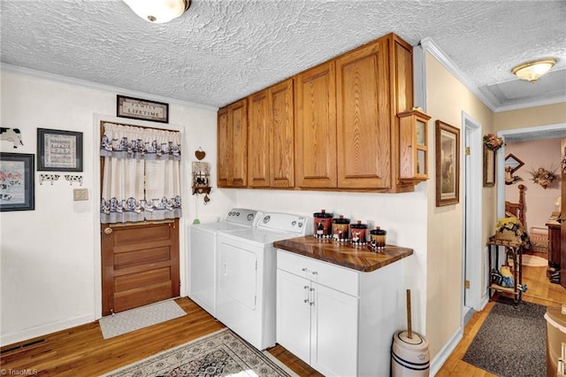 laundry area featuring cabinets, light wood-type flooring, a textured ceiling, washer and clothes dryer, and ornamental molding